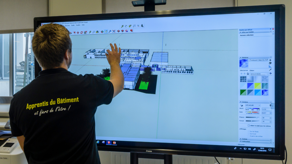 Un apprenant du BTS MEC (Management Économique de la Construction) travaille debout sur un écran tactile entrain de manipuler un plan numérique d'un bâtiment