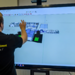 Un apprenant du BTS MEC (Management Économique de la Construction) travaille debout sur un écran tactile entrain de manipuler un plan numérique d'un bâtiment